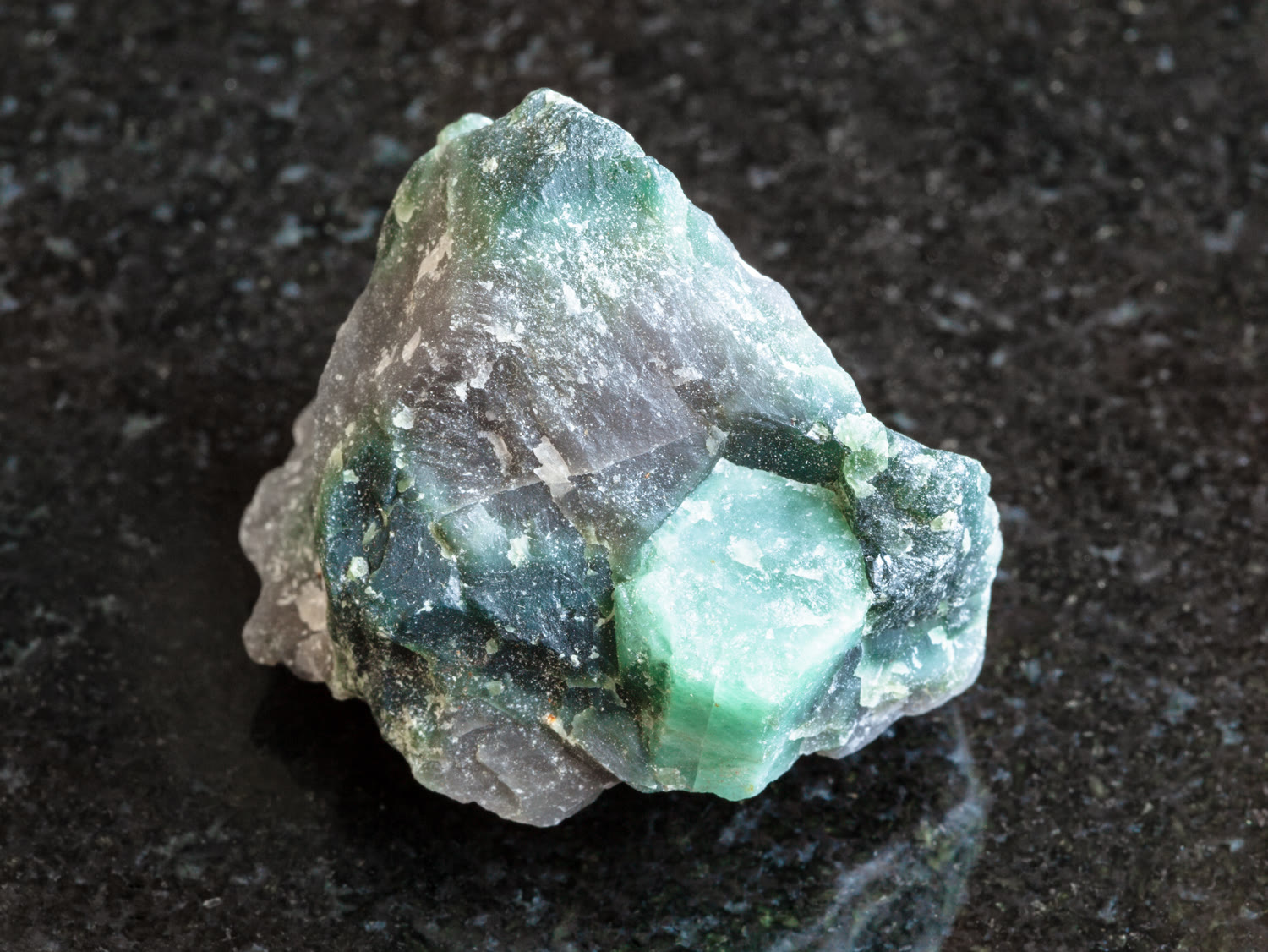 Cristallo di berillo grezzo verde incastonato nella roccia scura della matrice.